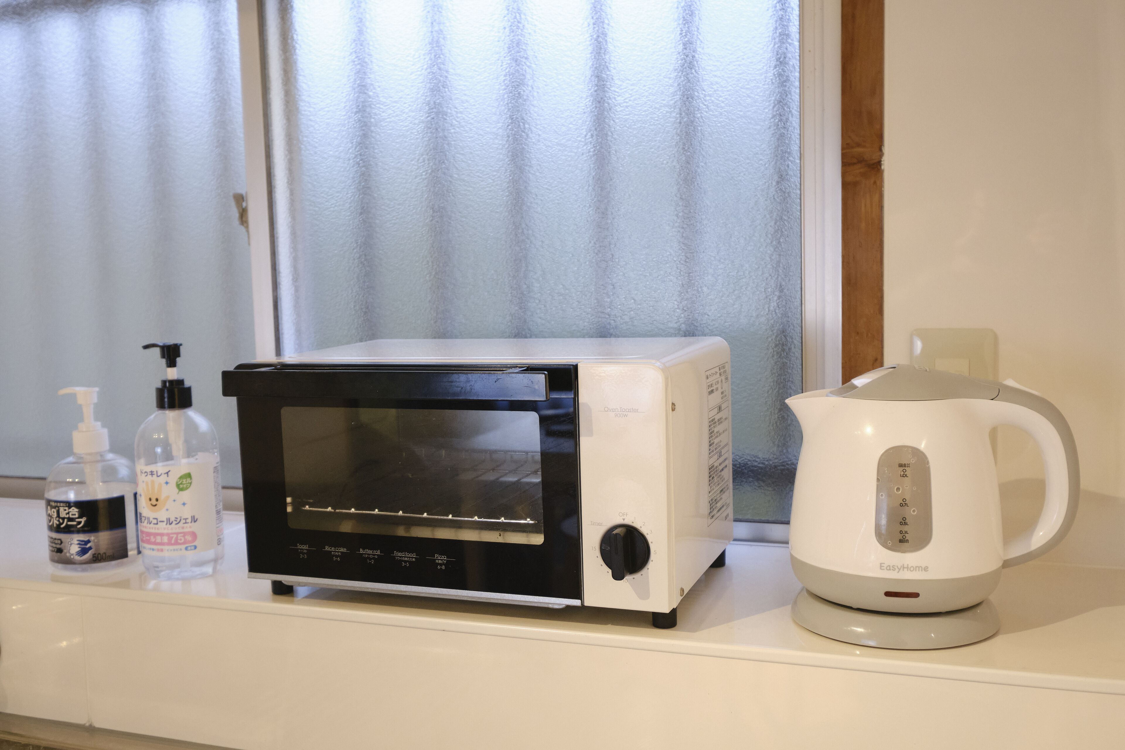 A kitchen with a microwave, a kettle, and two bottles of hand sanitizer on a counter.