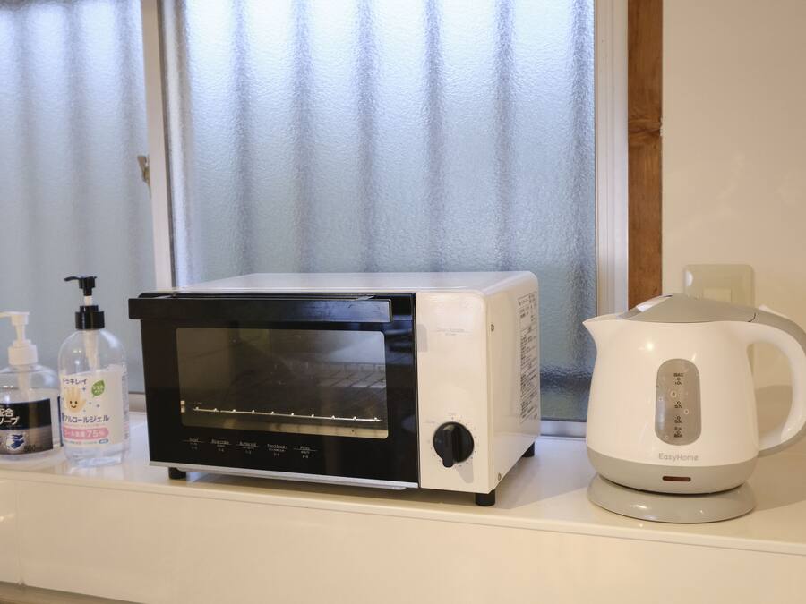 A kitchen with a microwave, a kettle, and two bottles of hand sanitizer on a counter.