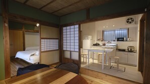 Een traditionele Japanse kamer met een tatami-mat vloer, een houten eettafel, een bed met een futon en een keukenhoek met een magnetron en spoelbak.