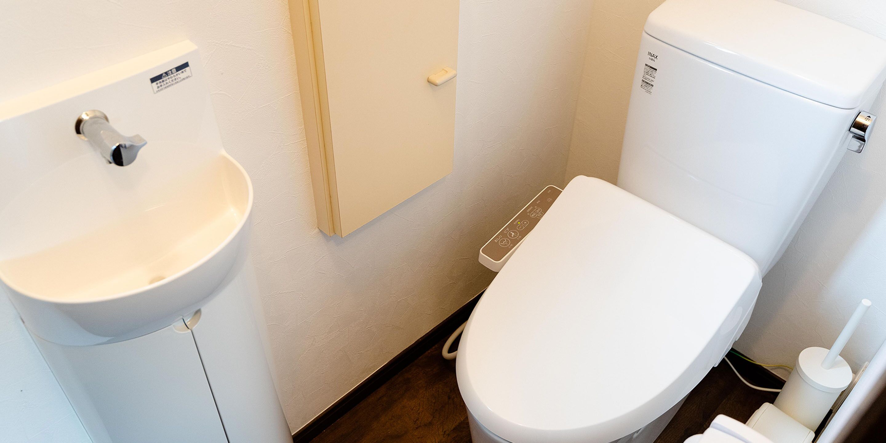A bathroom with a white sink, toilet, and a control panel on the wall.