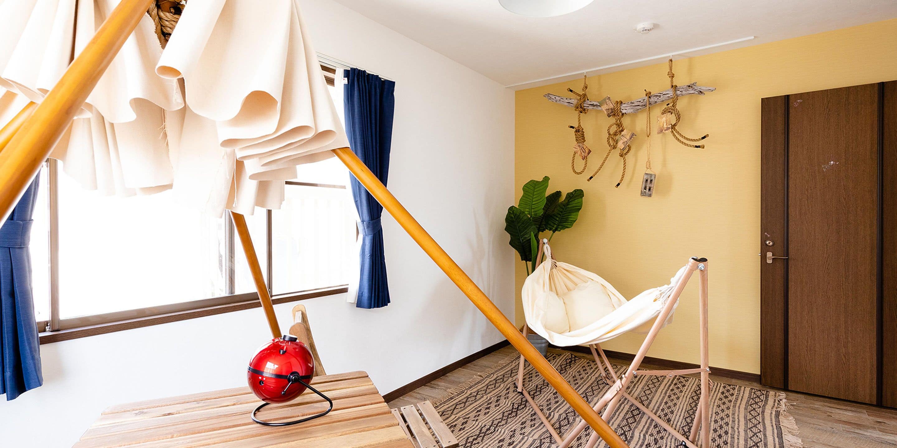 Una habitación con una silla hamaca, un aspirador rojo y suelo de madera.