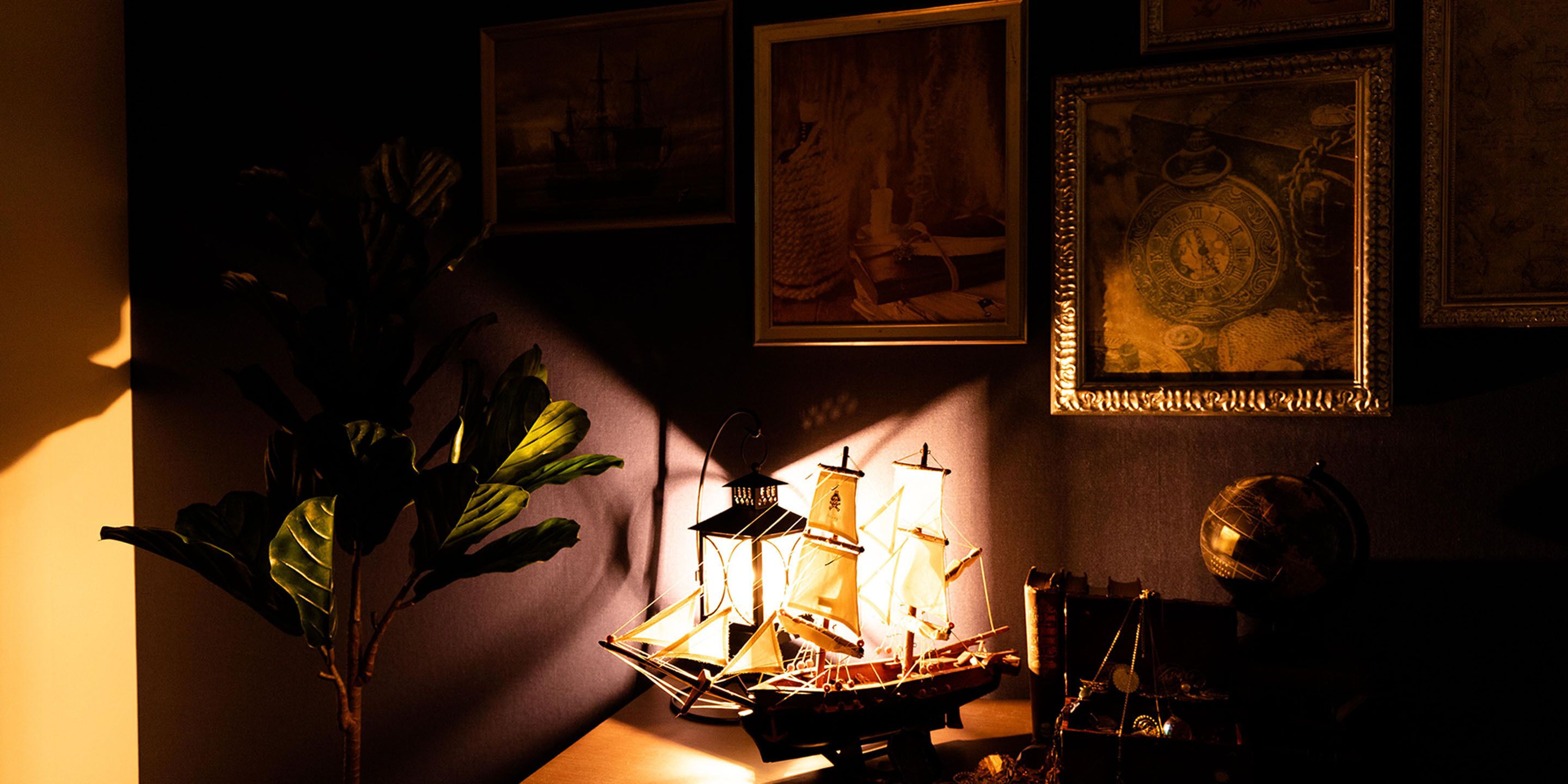 Una habitación con poca luz, un modelo de barco, un globo terráqueo y cuadros en la pared.