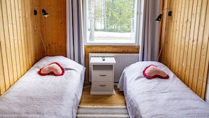Huoneessa on kaksi erillistä sänkyä, pieni valkoinen työpöytä, ikkuna, josta on näkymä puita kohti, ja puupaneeliseinät.