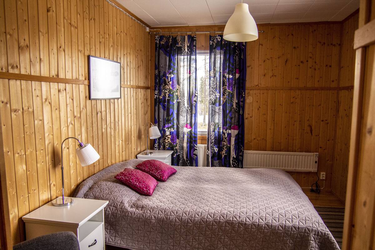 Un dormitorio con paneles de madera, una cama, mesitas de noche, un escritorio y una lámpara colgante.