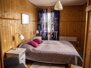 Ein Schlafzimmer mit Holzwandverkleidung, einem Bett, Nachttischen, einem Schreibtisch und einer Hängeleuchte.
