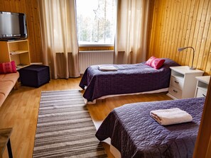 Ein Zimmer mit zwei Betten, einem Fernseher, einem kleinen Tisch und einem Fenster mit Vorhängen.