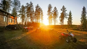 Soratie, jonka varrella on parkkeerattu maastoajoneuvoja, ja sen ympärillä kohoaa korkeita mäntyjä sekä näkyy rakennus, jonka katto on loivasti kalteva.