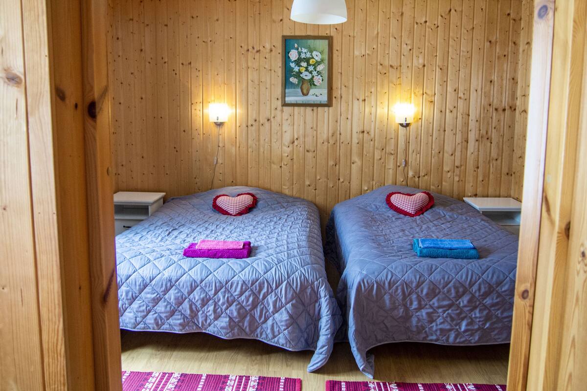 Una habitación con dos camas, cada una con un cojín con forma de corazón y una toalla doblada. Hay luces empotradas en la pared y un cuadro sobre las camas.