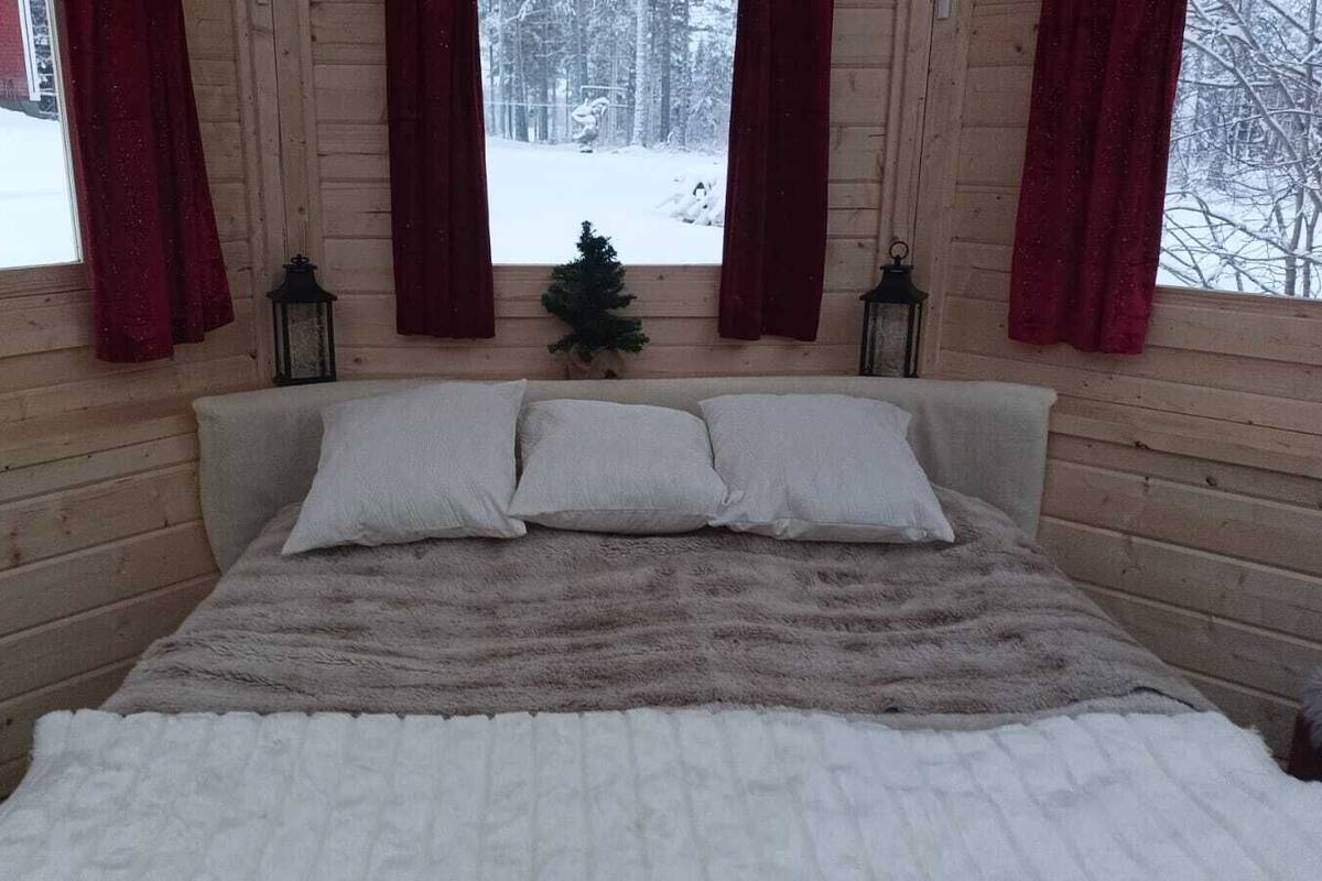 Un dormitorio acogedor tipo cabaña de madera, con una cama, dos almohadas y un pequeño árbol de Navidad.