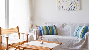 A living room with a white sofa, striped pillows, a wooden coffee table, and a painting of fish on the wall.