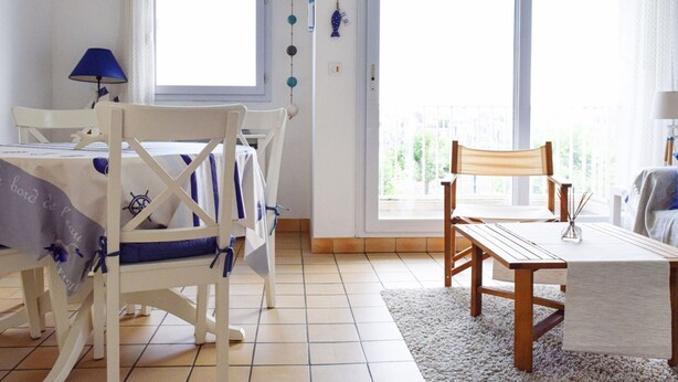 A room with a dining table, chairs, a sofa, and a balcony with a view.