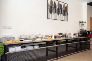 A buffet setup with various dishes, a coffee machine, and a decorative wall piece.