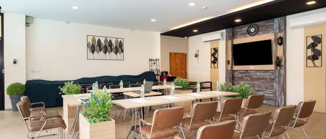 A conference room with tables, chairs, and a large screen.