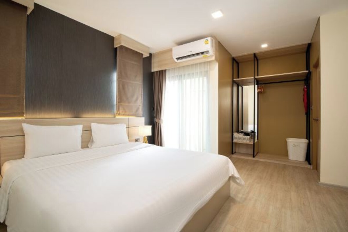 A hotel room with a large bed, an air conditioning unit, a walk-in closet, and a window with curtains.