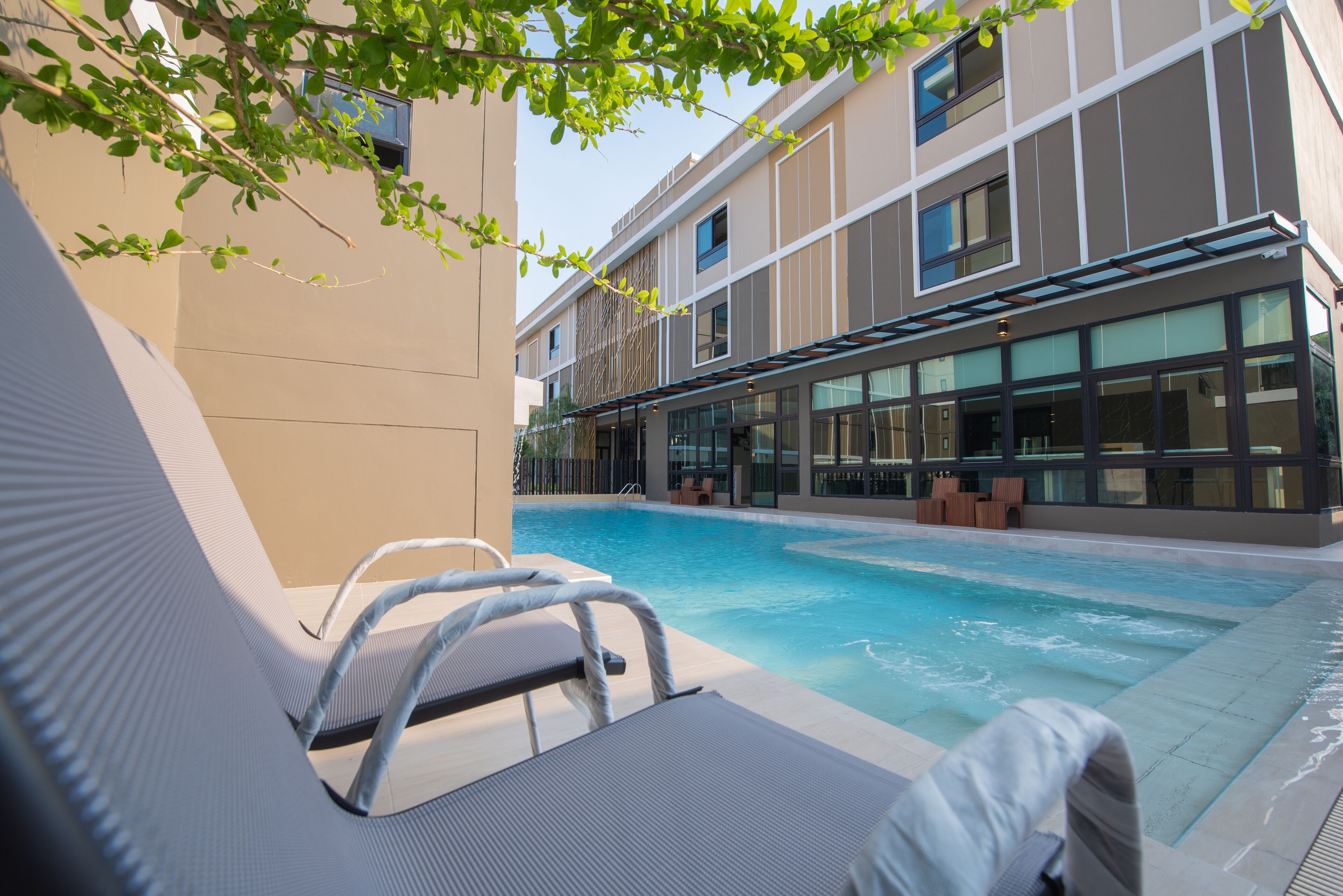 Zona de piscina con sillones de descanso y un edificio con amplias ventanas al fondo.