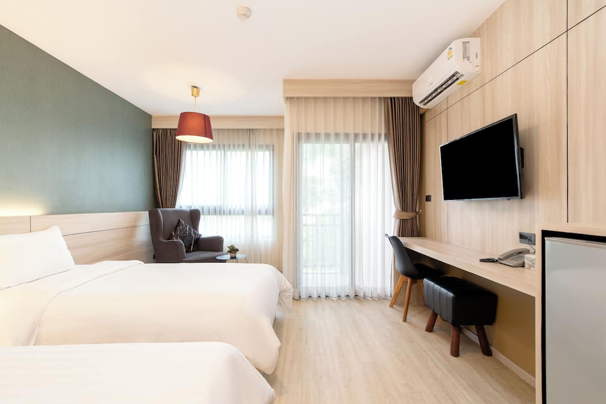 A hotel room with two beds, a desk, a chair, a television, and an air conditioning unit.