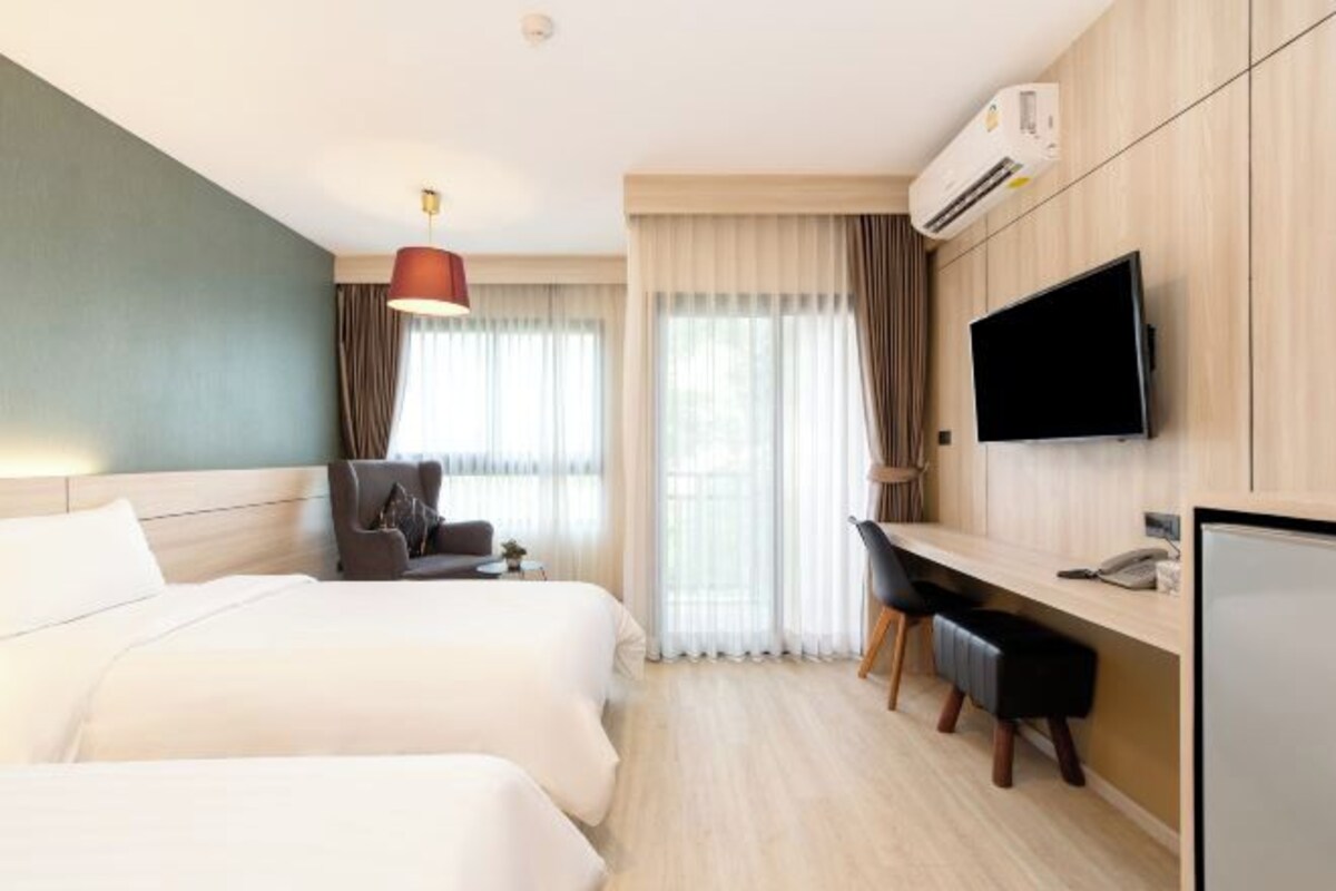 A hotel room with two beds, a desk, a chair, a TV, and an air conditioning unit.