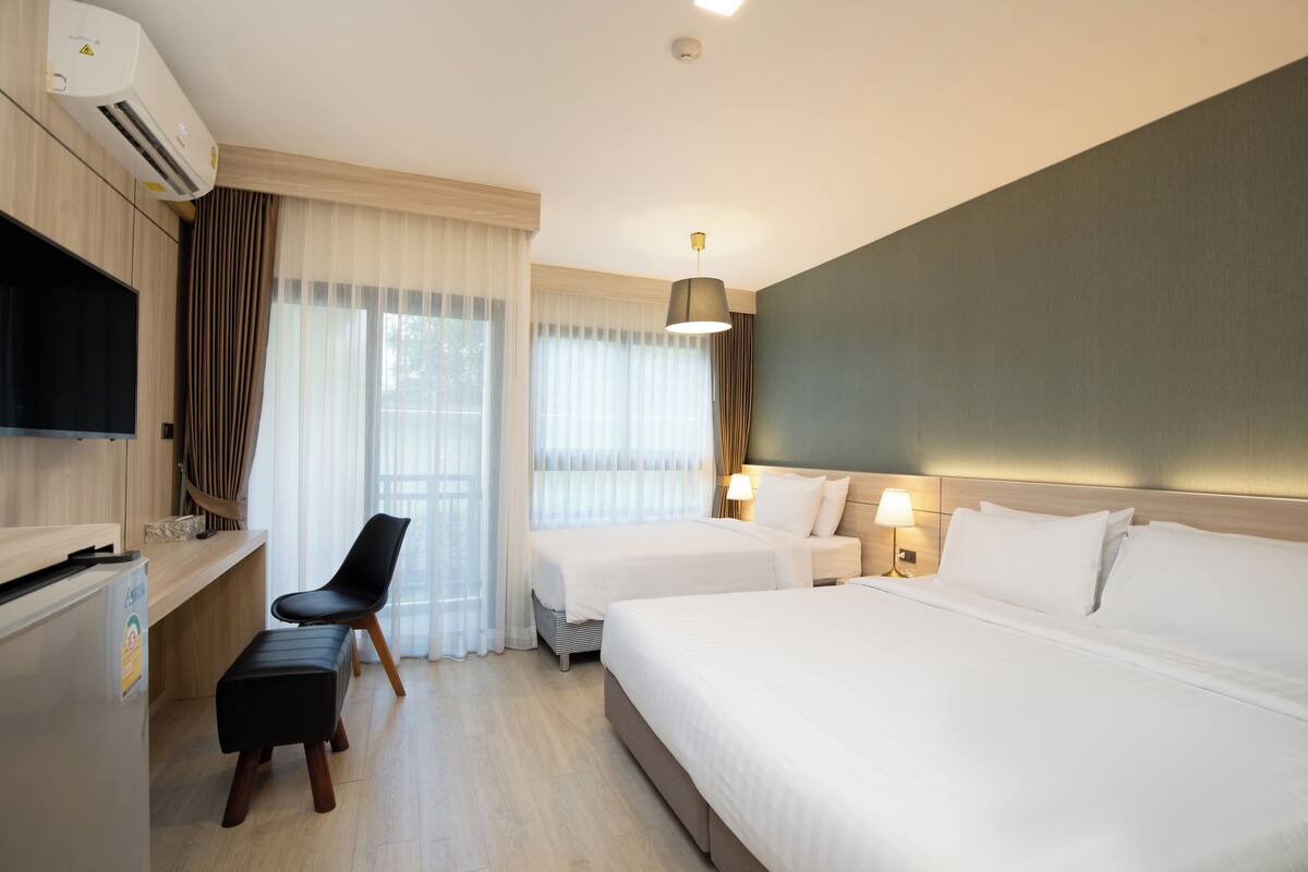 A hotel room with a bed, a desk, a chair, a TV, and a window with curtains.