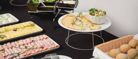 A buffet table with various food items including sliced meats, cheeses, and a salad.