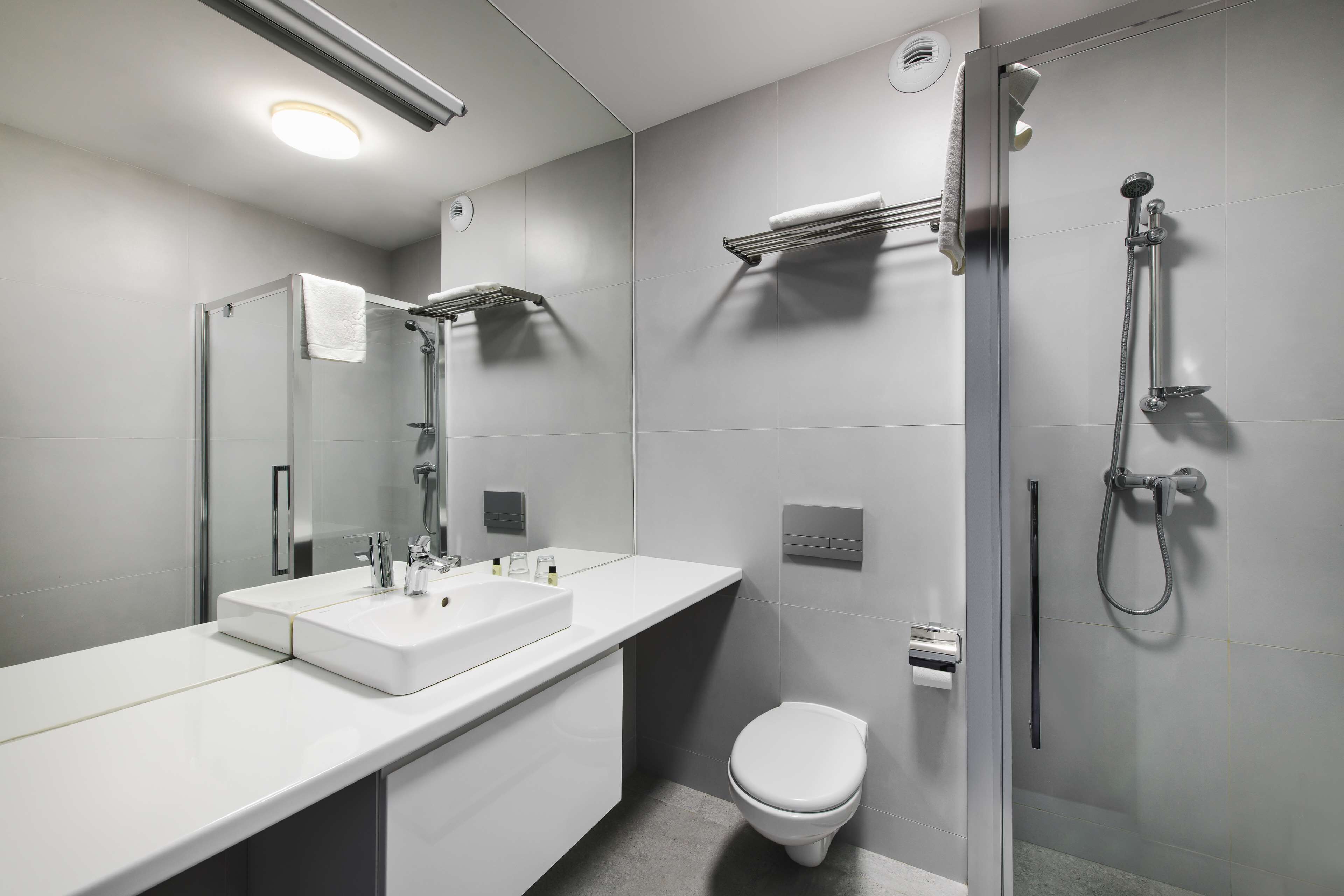 Un baño moderno con ducha de vidrio, un lavabo blanco con espejo y un inodoro.