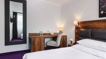 Une chambre d’hôtel comprenant un lit, un bureau avec une chaise, un miroir, une table de chevet avec une lampe et un tableau accroché au mur.