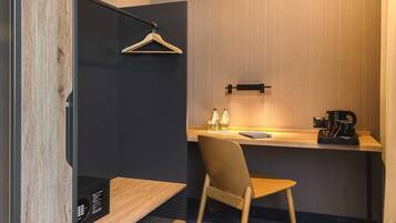 Una habitación de hotel moderna con un escritorio de madera, una silla, un perchero y un estante pequeño con botellas.