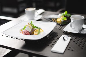 A dining table with a white plate of food, a white cup, and a spoon.