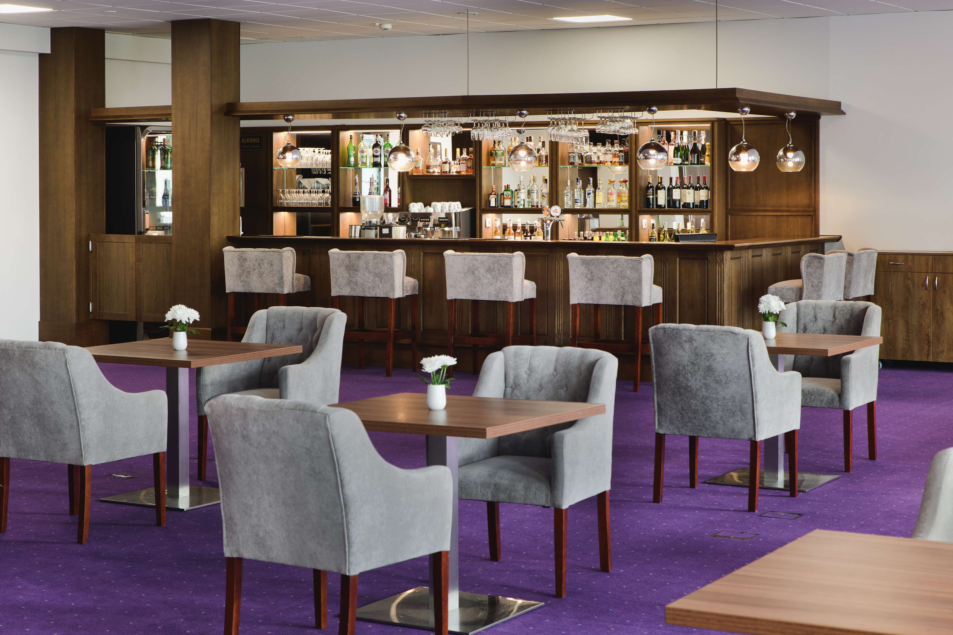 A bar area with multiple seating options, including bar stools and tables, and a variety of bottles and glasses on shelves.