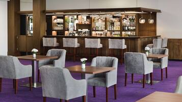 A bar area with multiple seating options, including bar stools and tables, and a variety of bottles and glasses on shelves.