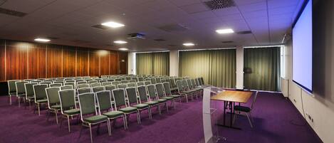 A conference room with rows of chairs, a podium, and a large screen.