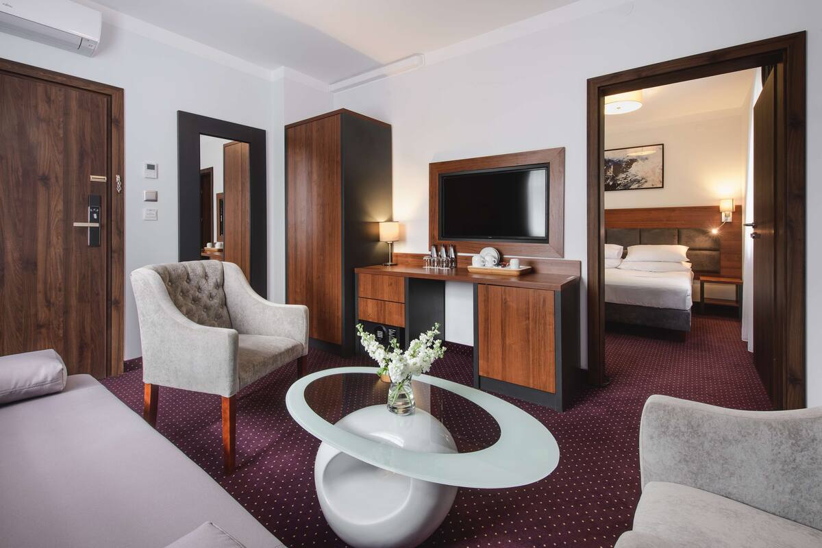 A hotel room with a bed, a desk with a flat-screen TV, a chair, and a coffee table.