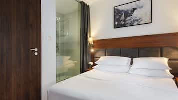 Ein Hotelzimmer mit einem Bett, einer Duschkabine aus Glas, einer Holztür und einem gerahmten Bild an der Wand.
