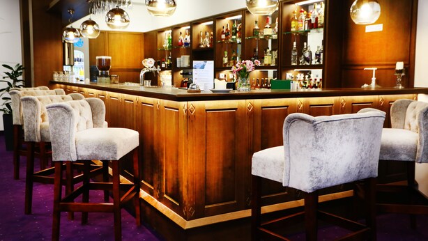 Zona de bar con mostrador de madera, taburetes y lámparas colgantes.