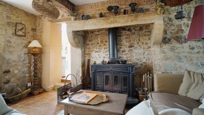 Une pièce rustique avec un mur en pierre, une table en bois sur laquelle repose un livre, un canapé et une cheminée avec une hotte.