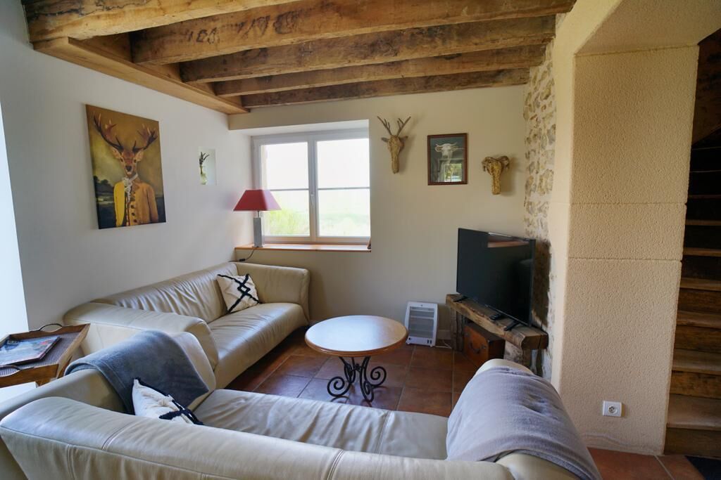 Un salón con sofá, una mesita redonda, televisión y ventana con persianas.