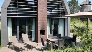 Una casa moderna con chimenea de ladrillo, ventanas amplias y mobiliario exterior.