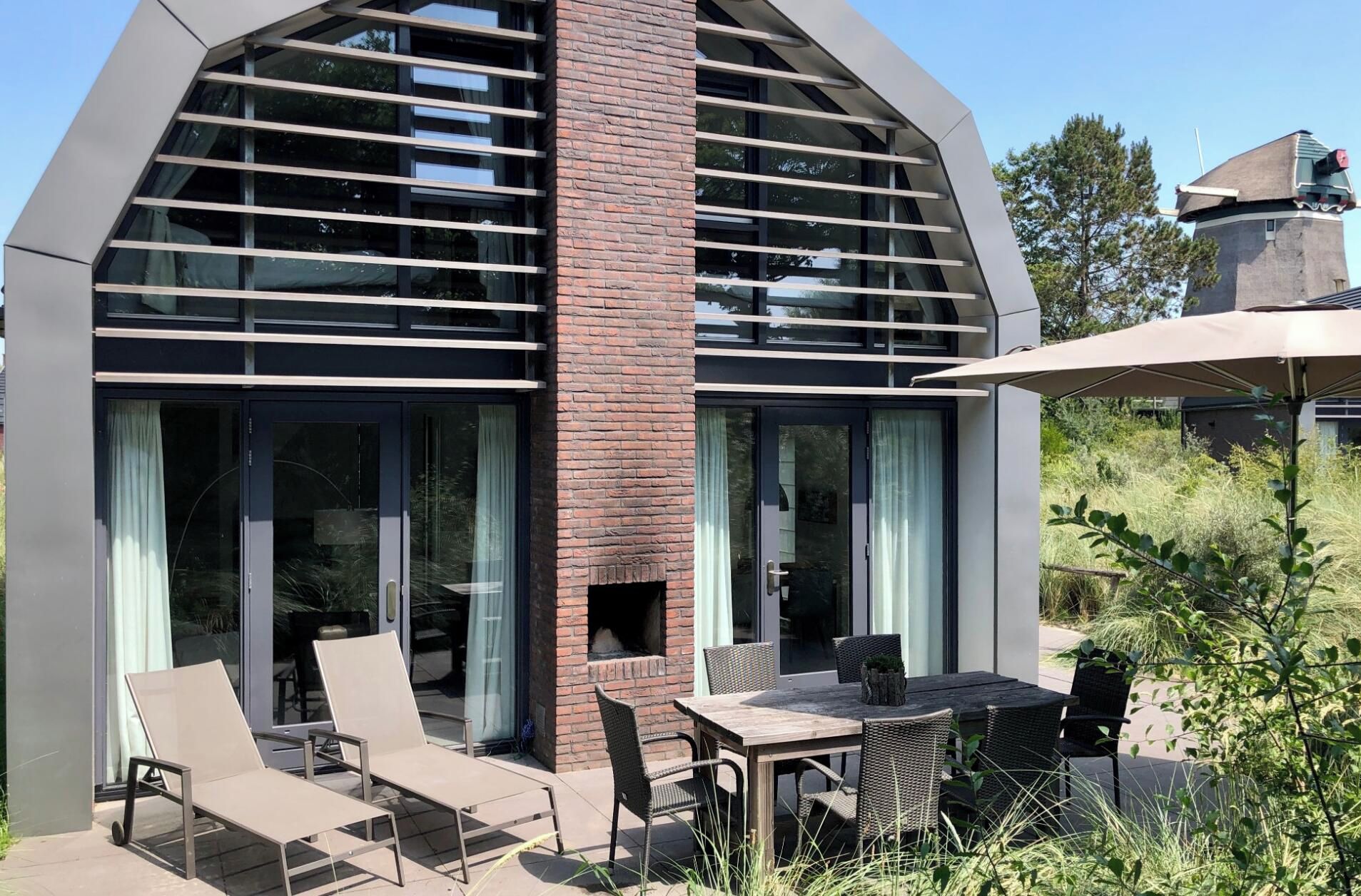 A modern house with a brick chimney, large windows, and outdoor seating.
