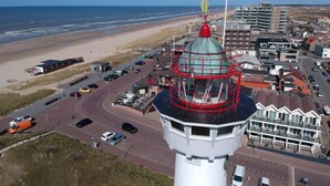 Un faro con estructura roja y blanca, una playa y una carretera con coches.