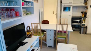 Une cuisine compacte équipée d’un four à micro-ondes, d’un four et d’un évier. On y trouve une table à manger avec des chaises, ainsi qu’un téléviseur posé sur un meuble.