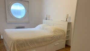 Une chambre à coucher avec un lit, une fenêtre ronde, une table de chevet avec deux lampes et une étagère intégrée.