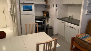 Une cuisine compacte équipée d’un four à micro-ondes, d’un four et d’un lave-vaisselle. On y trouve une table à manger avec des chaises et une poubelle.