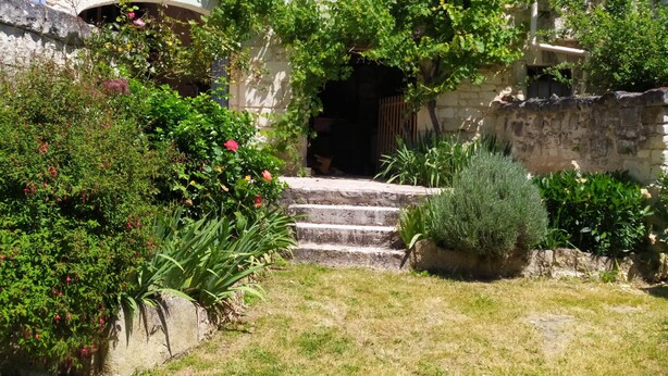 A stone building with a rustic entrance, steps leading up to a doorway, and lush greenery surrounding the structure.
