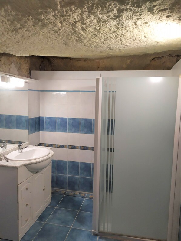 Une salle de bain avec un lavabo blanc, des murs recouverts de carreaux bleus et une cabine de douche en verre.