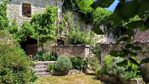 A stone building with a garden area featuring steps leading to a door, surrounded by various plants and shrubs.