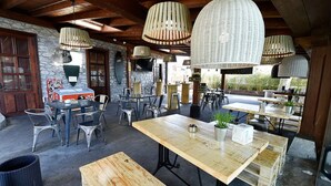 An outdoor dining area with rustic wooden tables and chairs, stone walls, and hanging wicker lamps. - Posada Término (Entrambasaguas)