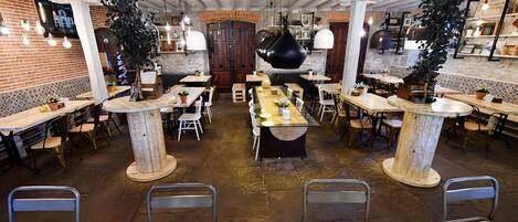 A restaurant with multiple tables and chairs, featuring a rustic brick wall and exposed ceiling beams.