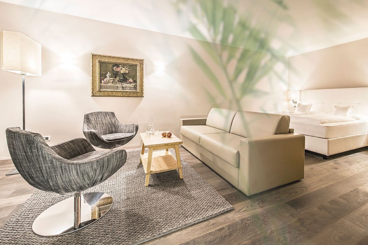 A modern living room with a sofa, armchair, coffee table, and a bed with a headboard.