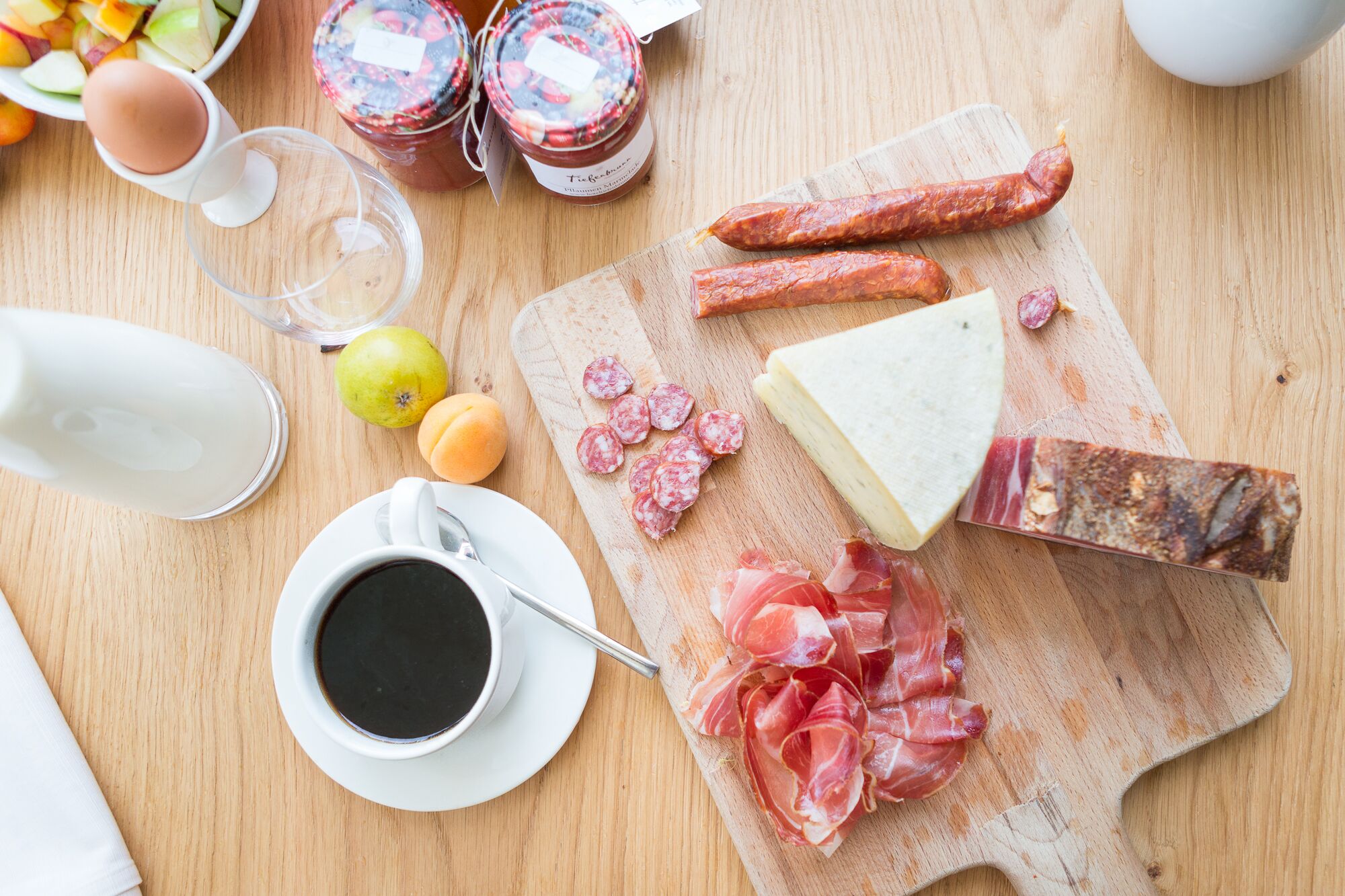 Ein Holztisch mit Käse, Wurstwaren, einem Messer und einer Kaffeetasse.