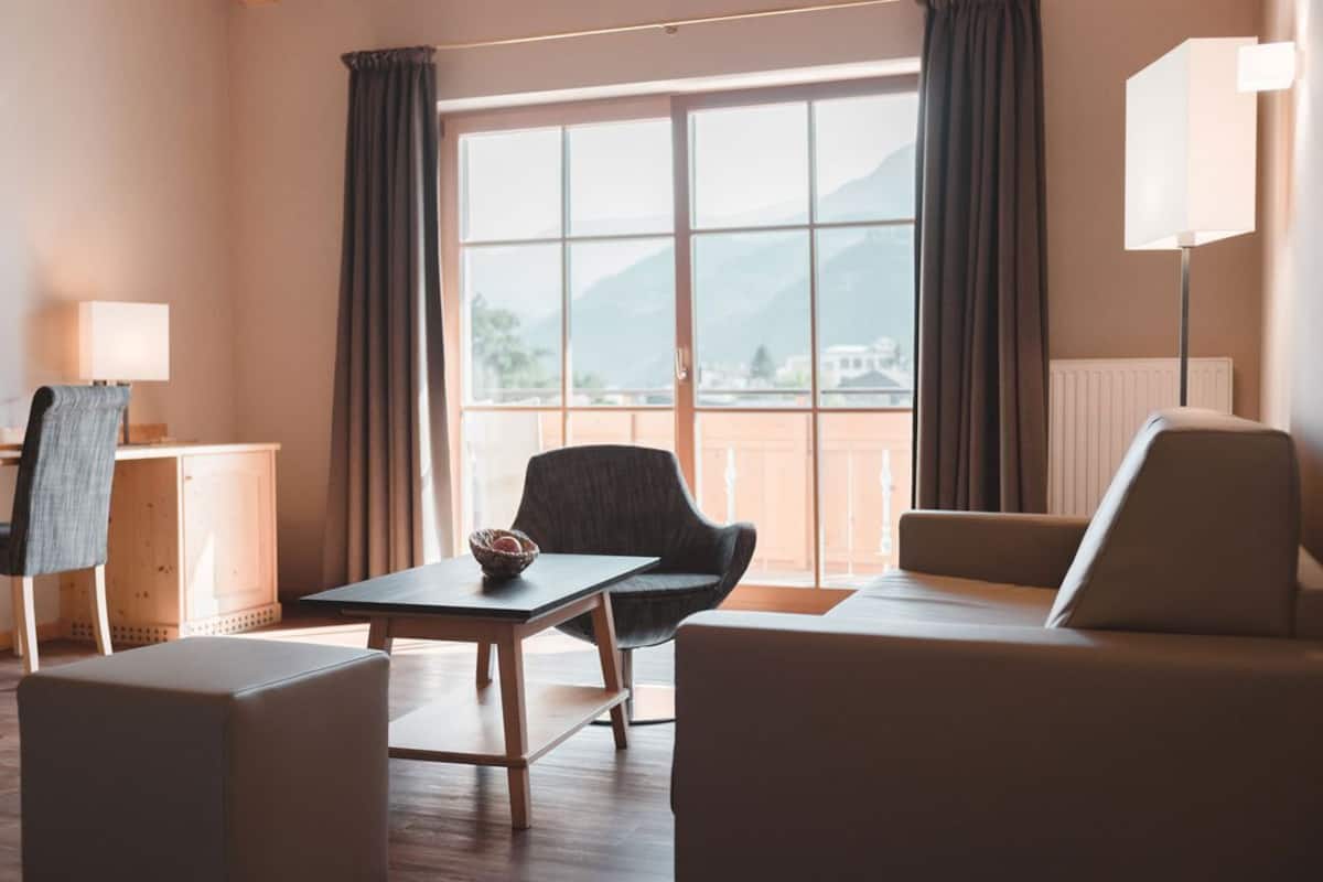 A hotel room with a large window, a sofa, a chair, a table, and a lamp.
