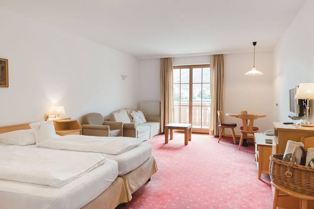 A hotel room with two beds, a sofa, a dining table, and a TV.